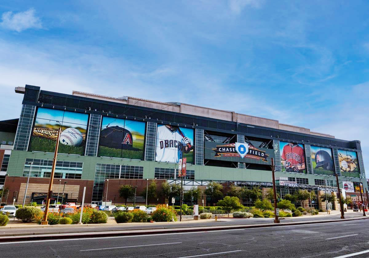 A green stadium with giant windows that have baseball imagery on them. In the center of the building the words “Chase Field”