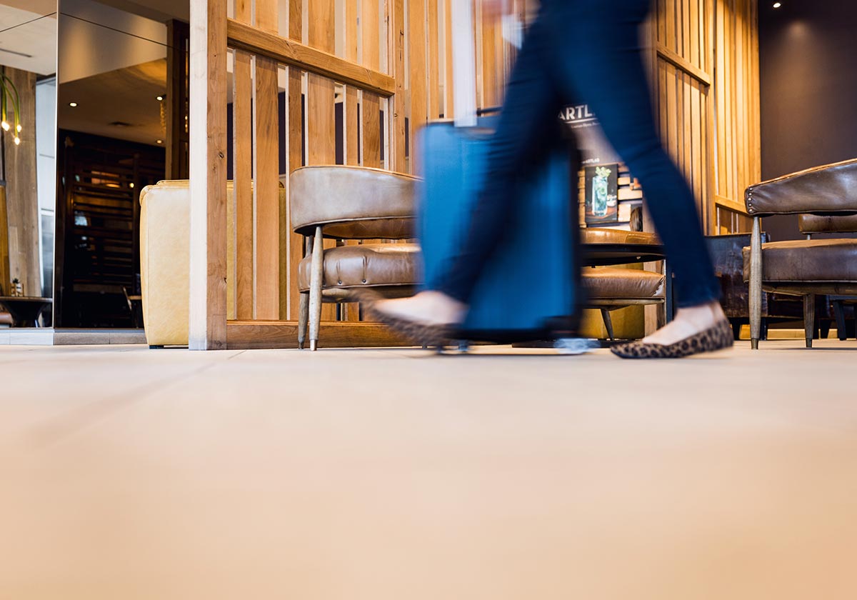 A woman walking across a beige and brown lobby of a hotel.