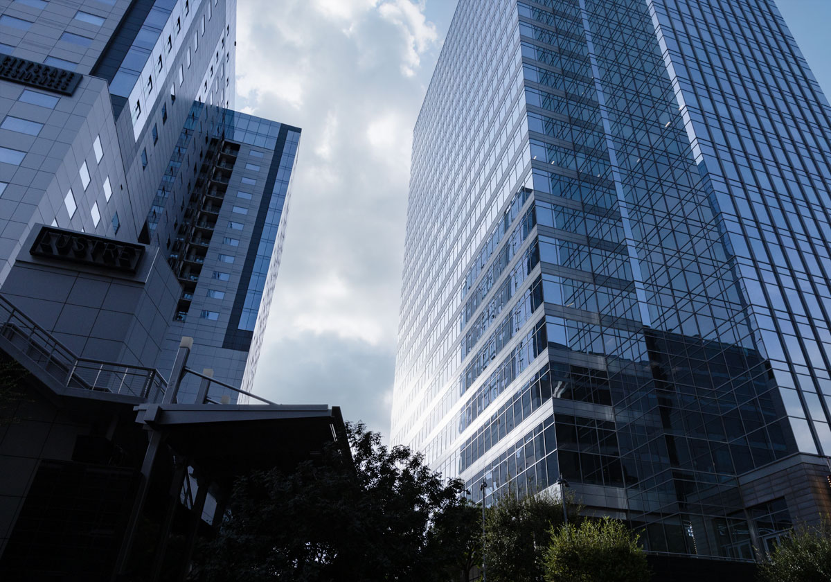 Three skyscrapers with trees at the bottom rising into a cloudy gray sky.